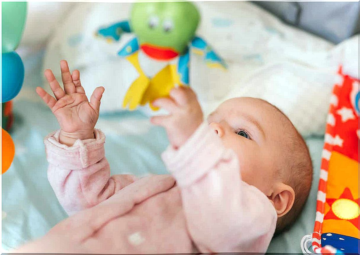 A girl lying in a crib and playing with a baby gym.