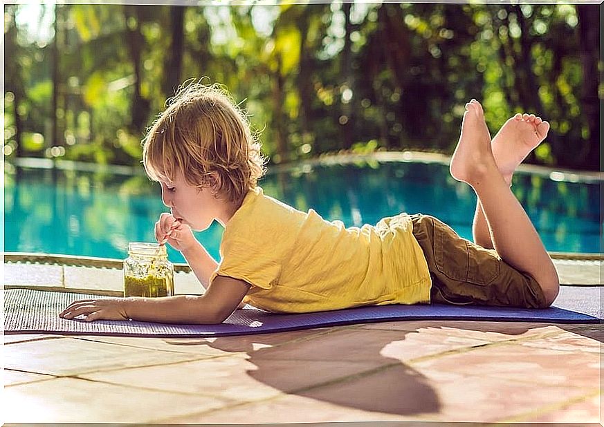 children lie on the ground in front of a pool and drink green juice