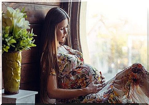 Fear of giving birth: pregnant woman sitting in window holding her stomach