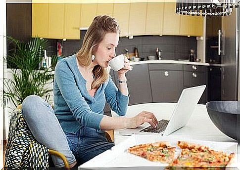 woman drinking coffee and working on computer, there is a pizza next to her