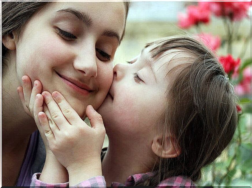 toddler with downs syndrome kissing cheek on older sister