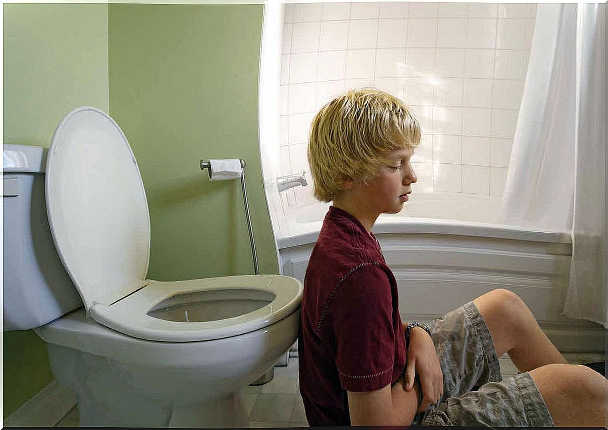 A teenager sitting on the floor in the bathroom and looking sick.