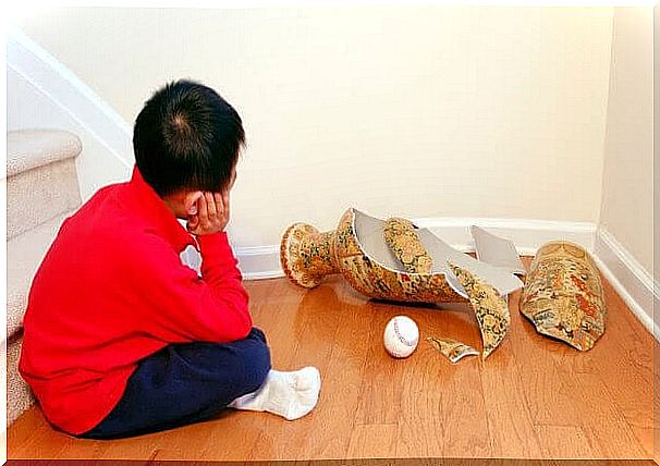 Boy sitting on the floor next to a broken vase and a ball