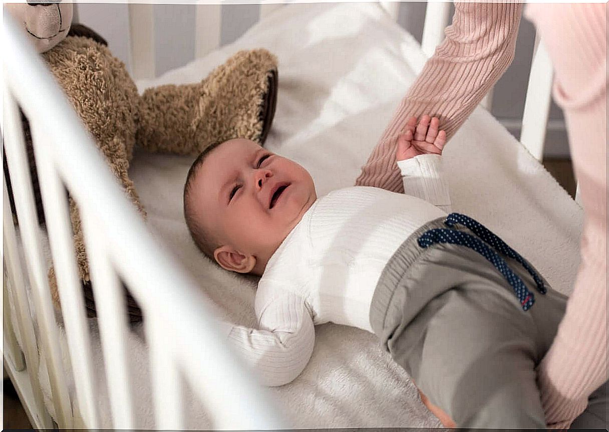 A mother picks up her crying baby from her crib.