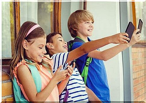 Children stand in line and look at their smartphones - two take selfies