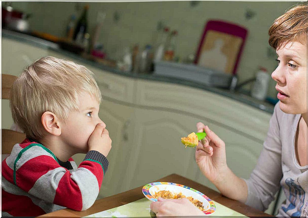 A small child covering his mouth while his mother tries to feed him.