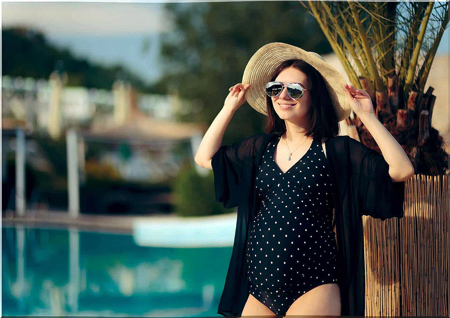 A pregnant woman standing in the sun by a pool.