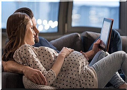 man and pregnant woman on sofa looking at tablet