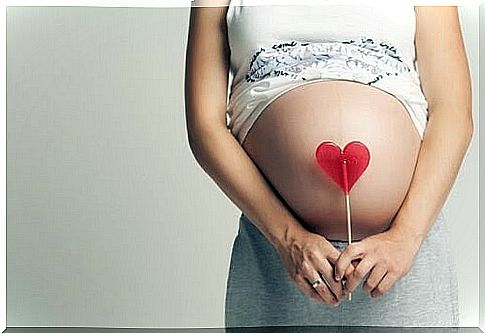 Highly pregnant woman holding a heart-shaped candy cane