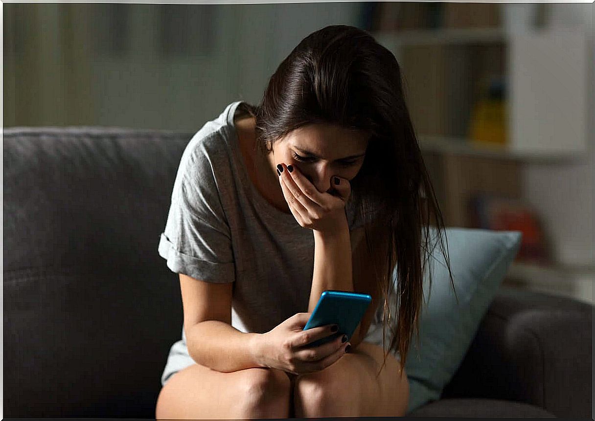 A teenager looks at her phone with her hand over her mouth.